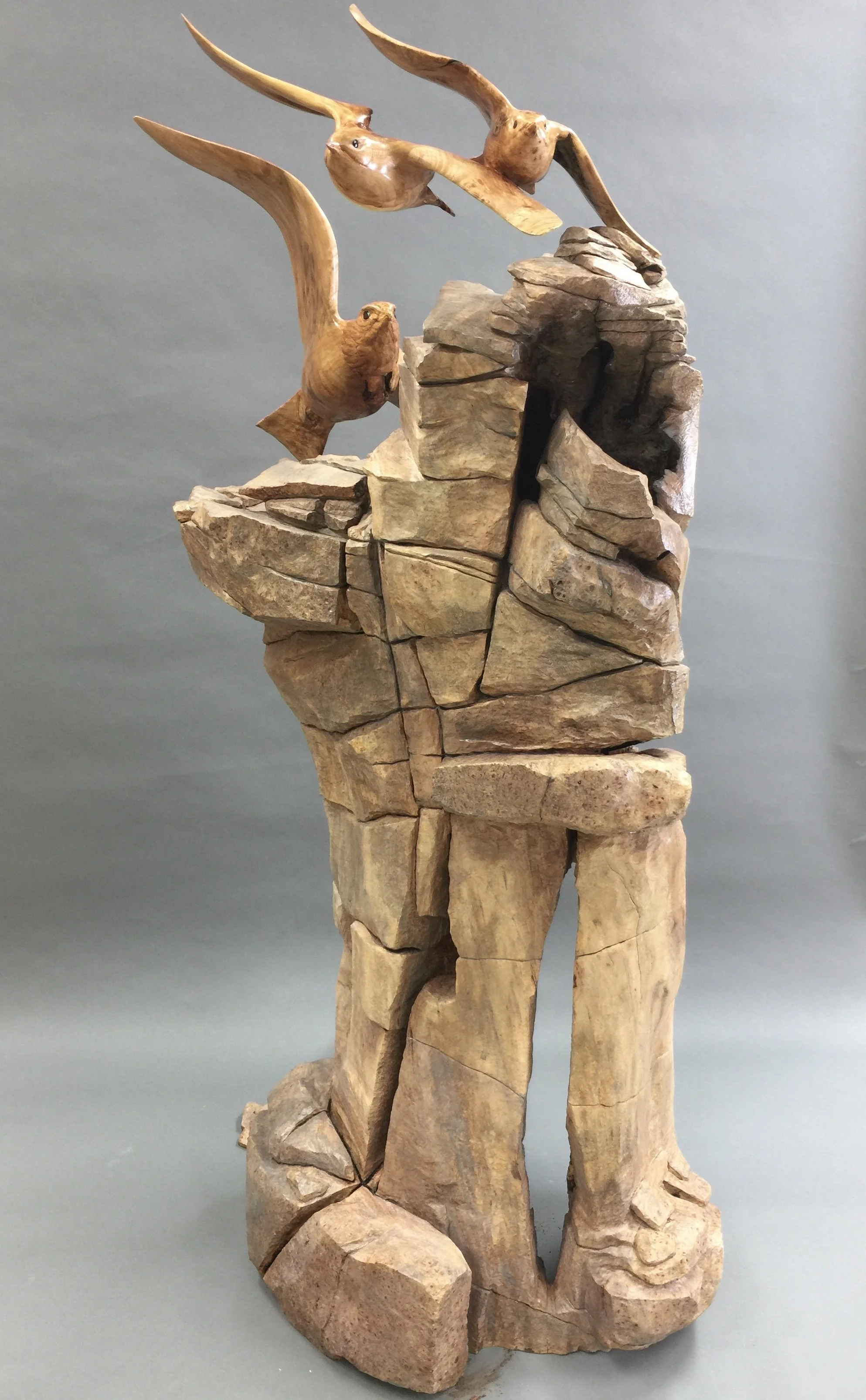 Wooden sculpture of an eagle and three birds perched on a rocky base