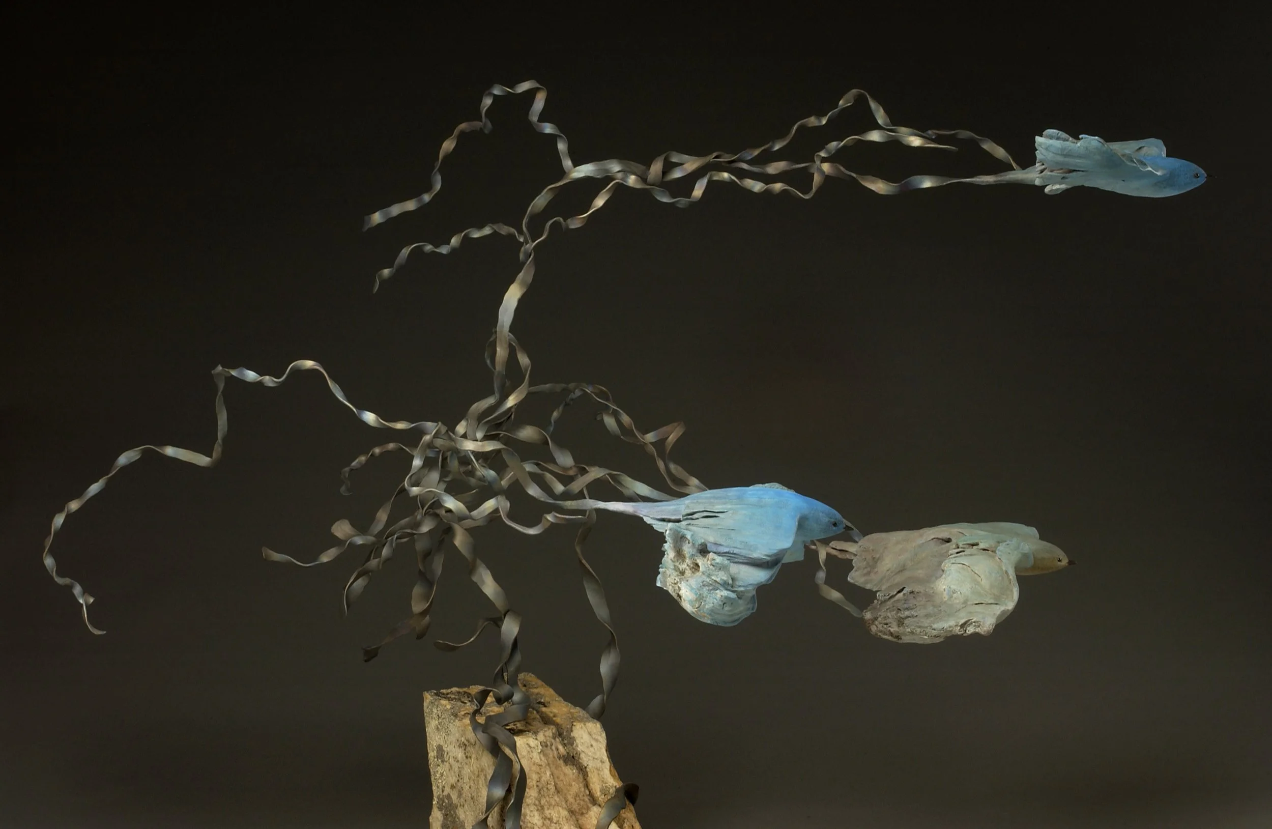 Sculpture of two fish with twisted metal fins and a rock base on a black background.
