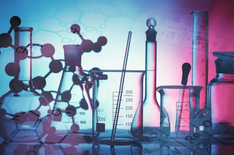 Laboratory glassware including beakers, test tubes, and a graduated cylinder with chemical structures and formulas overlayed in the background.
