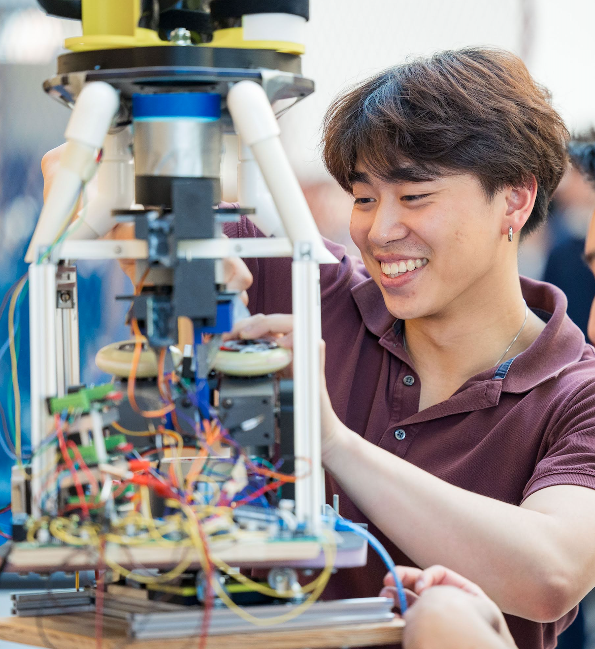 Young man assembling or working on a robotic device with exposed wiring and mechanical parts.