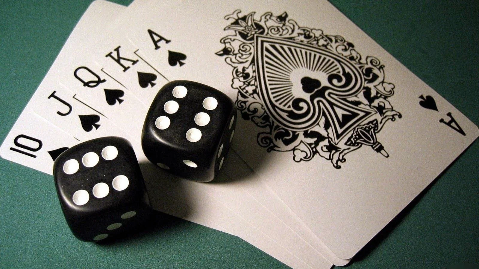 A hand of playing cards showing ten, Jack, Queen, King, Ace of Spades, and a large pair of black dice with white dots, all laid out on a green surface.