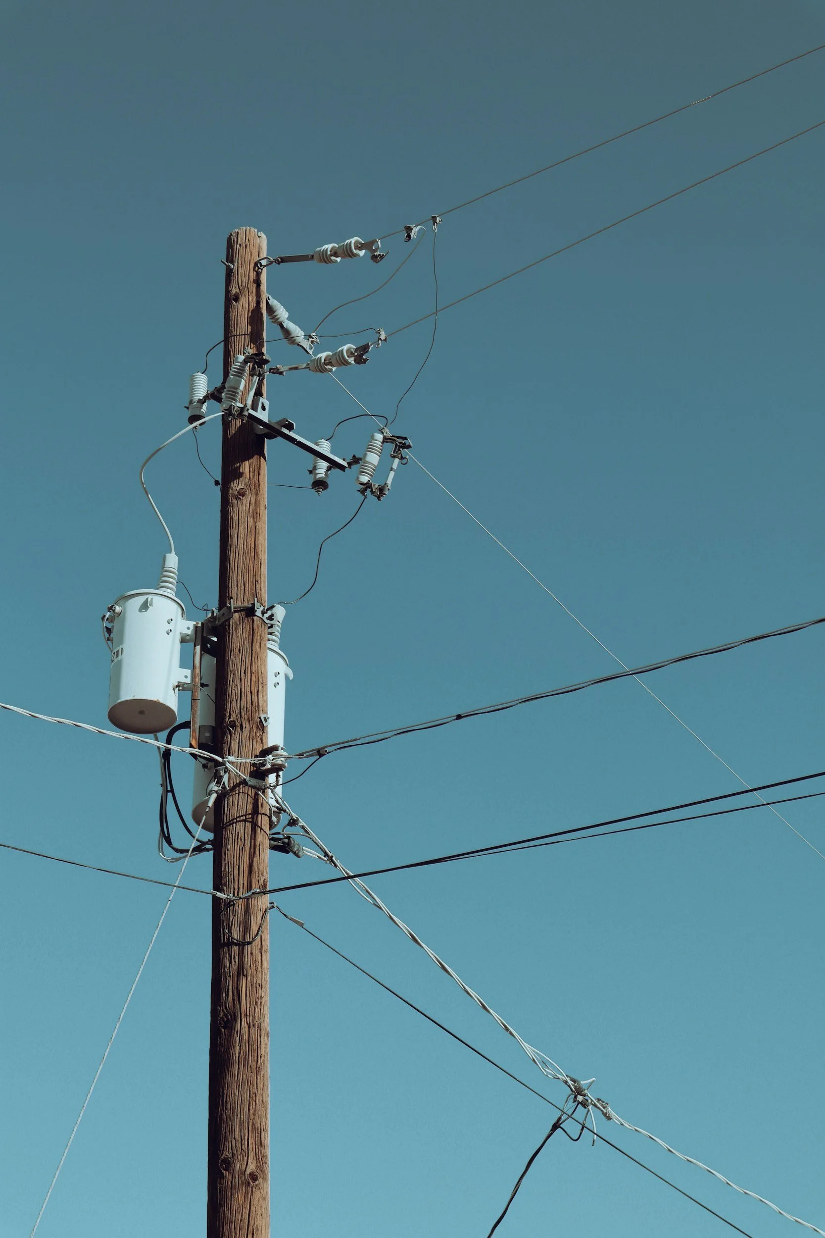 A wooden utility pole with multiple electrical wires and insulators against a clear blue sky.