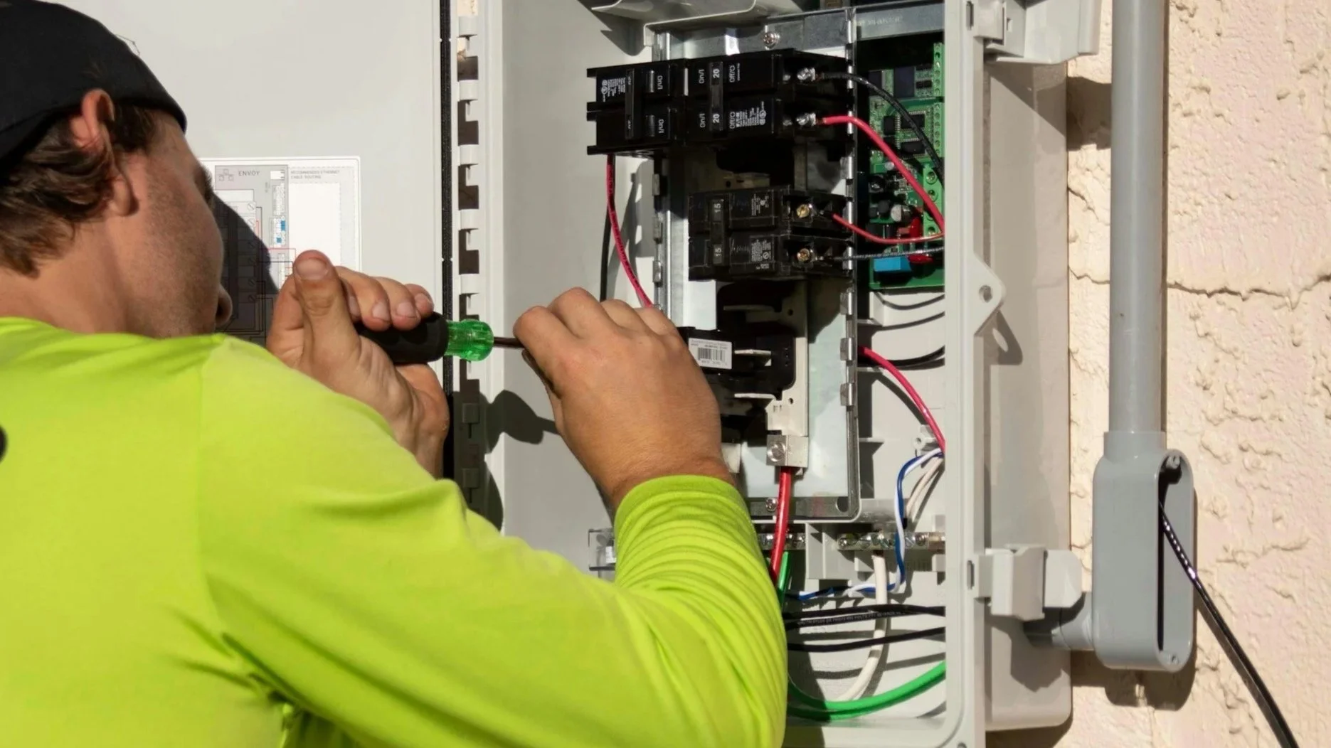 Electrician working inside an electrical panel or breaker box with a screwdriver.