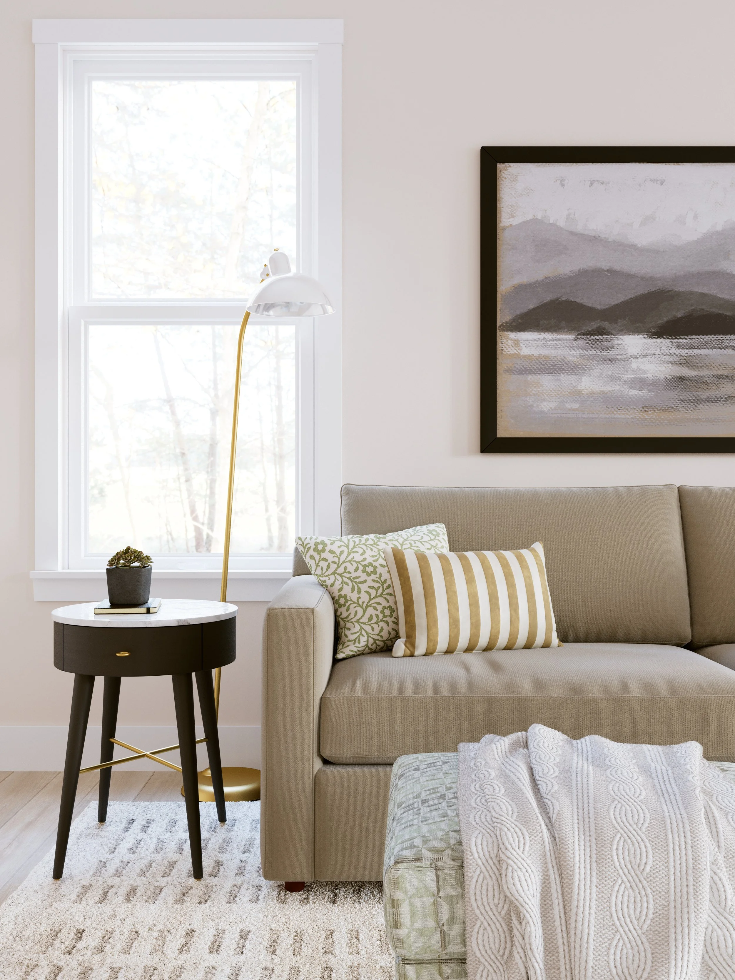 A cozy living room corner with a beige sofa, decorative pillows, a black side table with a plant, a white and gold floor lamp, a window with white trim, and a framed landscape painting of mountains.