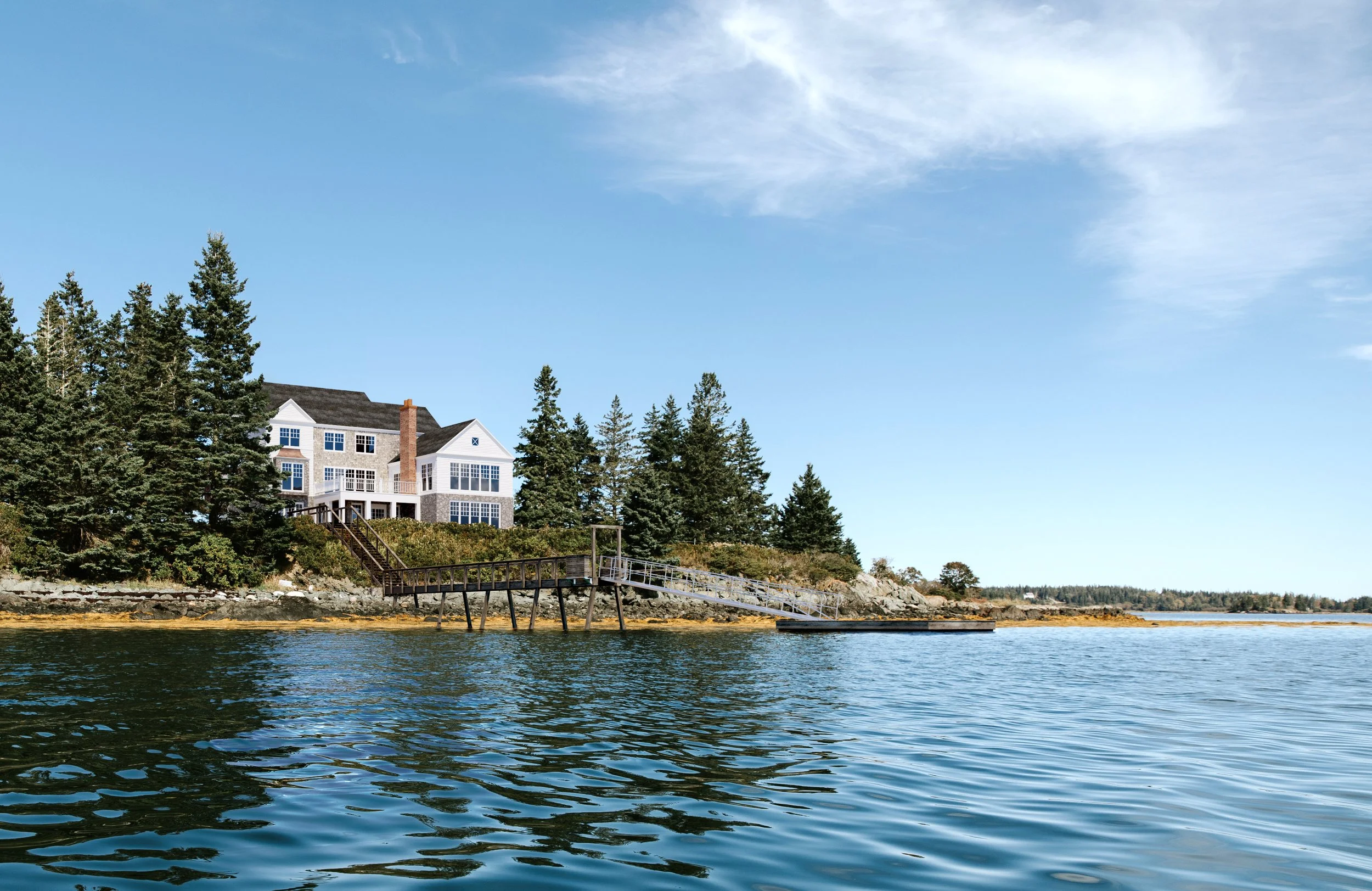 A house with white siding and a chimney, situated on a wooded hillside overlooking a body of water. There is a dock extending into the water, and tall evergreen trees surround the house. The sky is mostly clear with some wispy clouds.