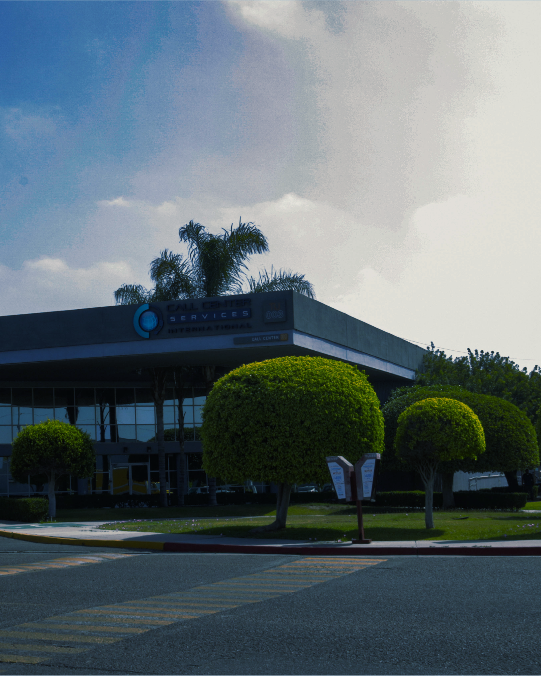 Exterior view of a call center services building with well-manicured trees and a clear sky.