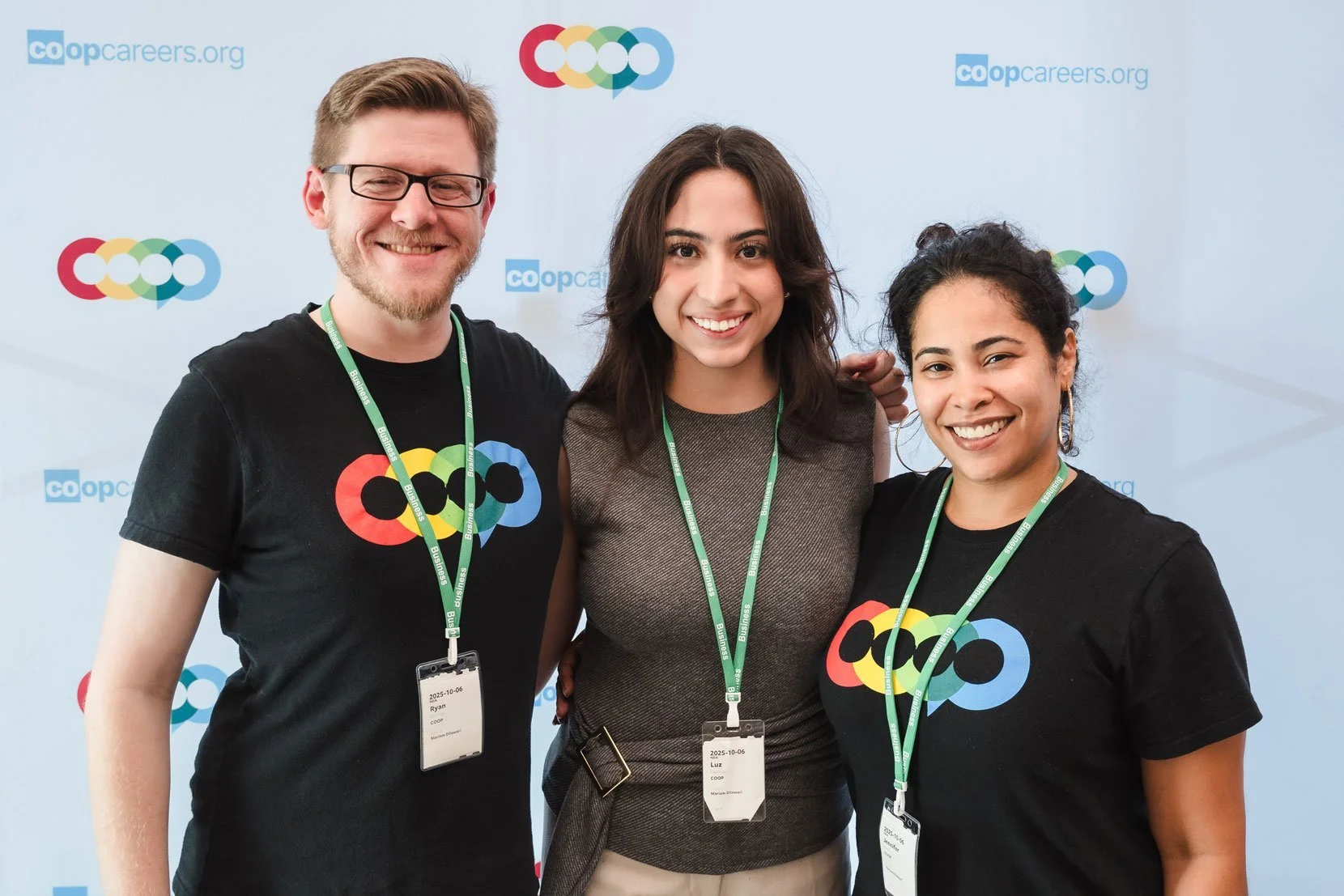 Three smiling people posing together at a conference or event, wearing guest badges and black T-shirts with a colorful logo, standing in front of a background with the 'co-opcareers.org' logo and a multicolored overlapping circle design.