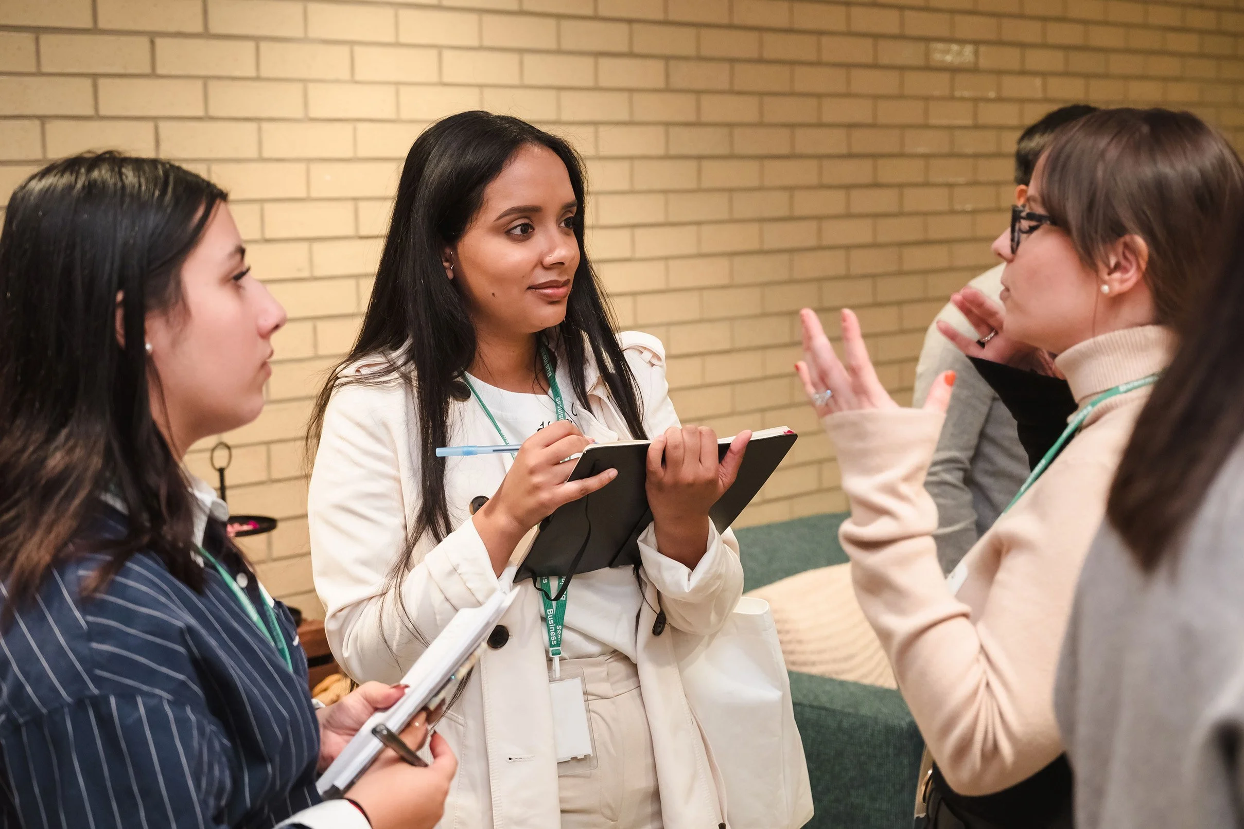 Group of women engaged in conversation at a professional event, standing in front of a brick wall.