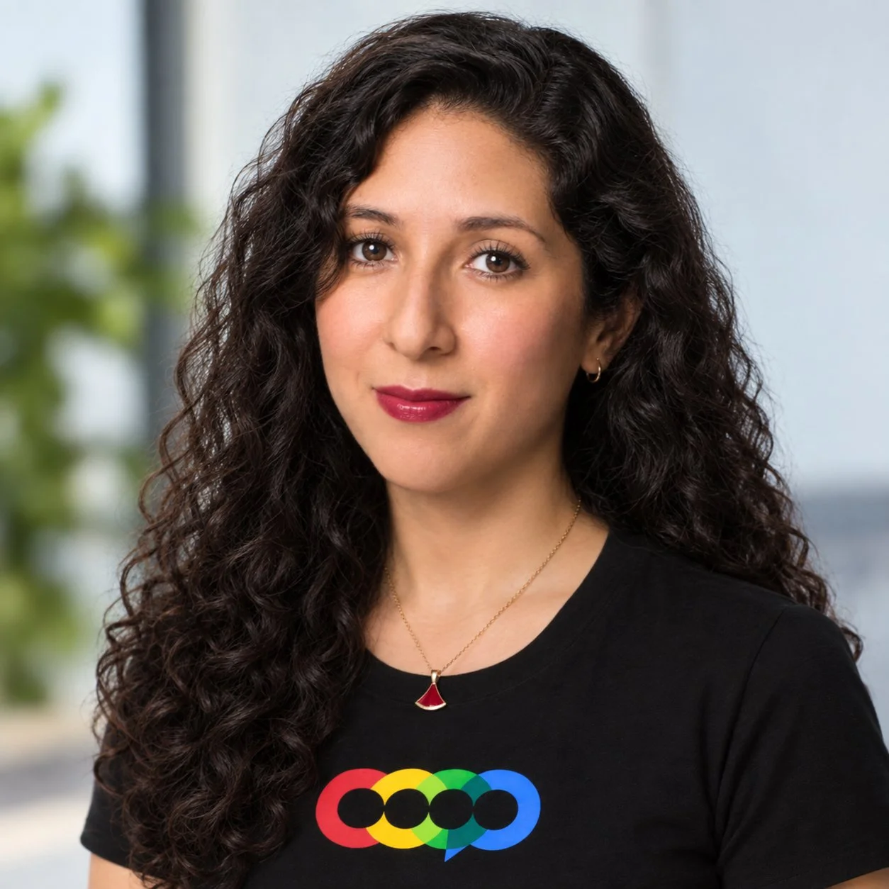 Woman with long dark curly hair wearing a necklace and black shirt with a colorful logo