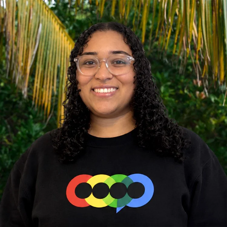 Woman with dark curly hair wearing clear glasses against a tropical background