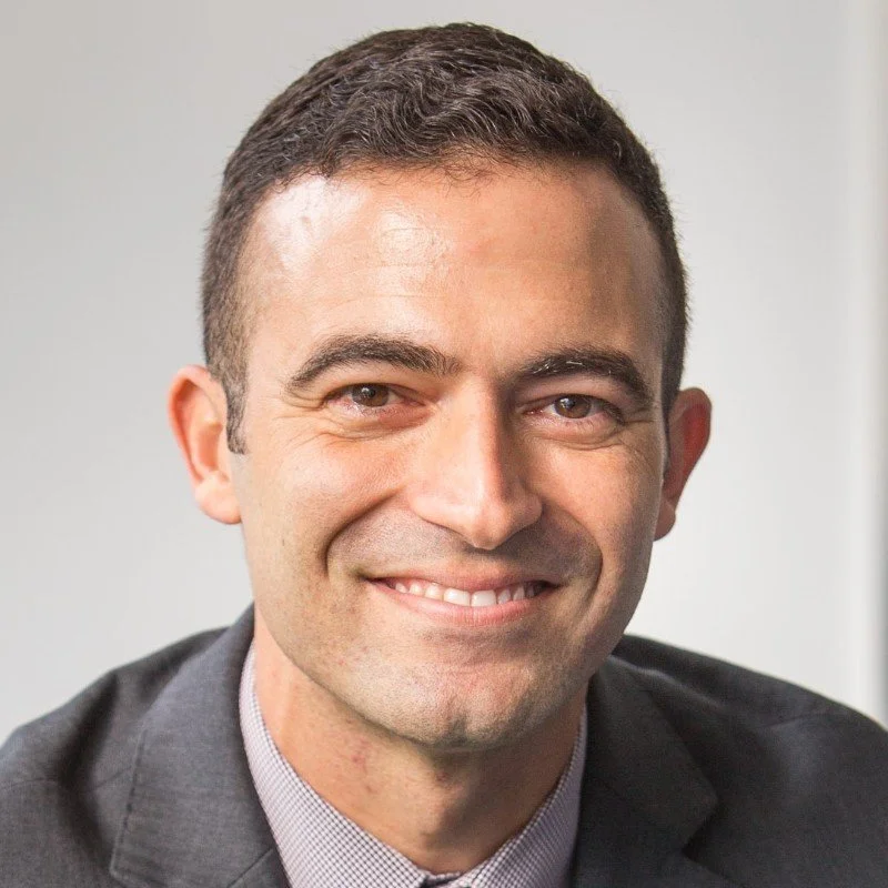 Close-up of a smiling man in a business suit with a neutral background.
