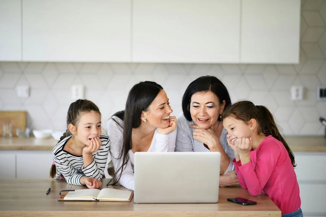 Family gathered around a laptop at the kitchen counter, smiling and engaging with each other.