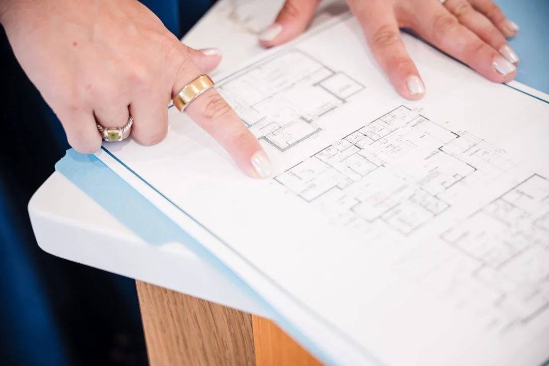 Person pointing at a blueprint or architectural plan with two fingers, on a wooden surface.