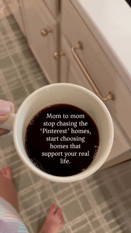 Close-up of a coffee mug with text that reads, "Mom to mom stop chasing the 'Pinterest' homes, start choosing homes that support your real life." The mug is being held over a kitchen floor with a cabinet in the background.