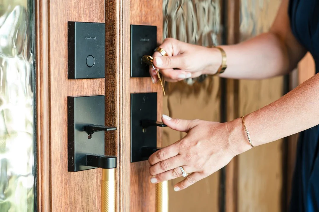 A person inserting a key into a lock on a wooden door with a black handle and multiple black switch plates.