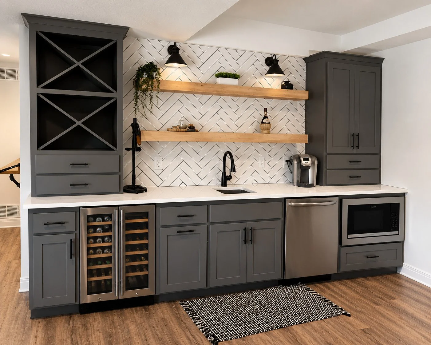 Kitchen with gray cabinets, white countertop, black fixtures, wooden open shelves, wine fridge, microwave, and small black and white patterned rug, with wood flooring.