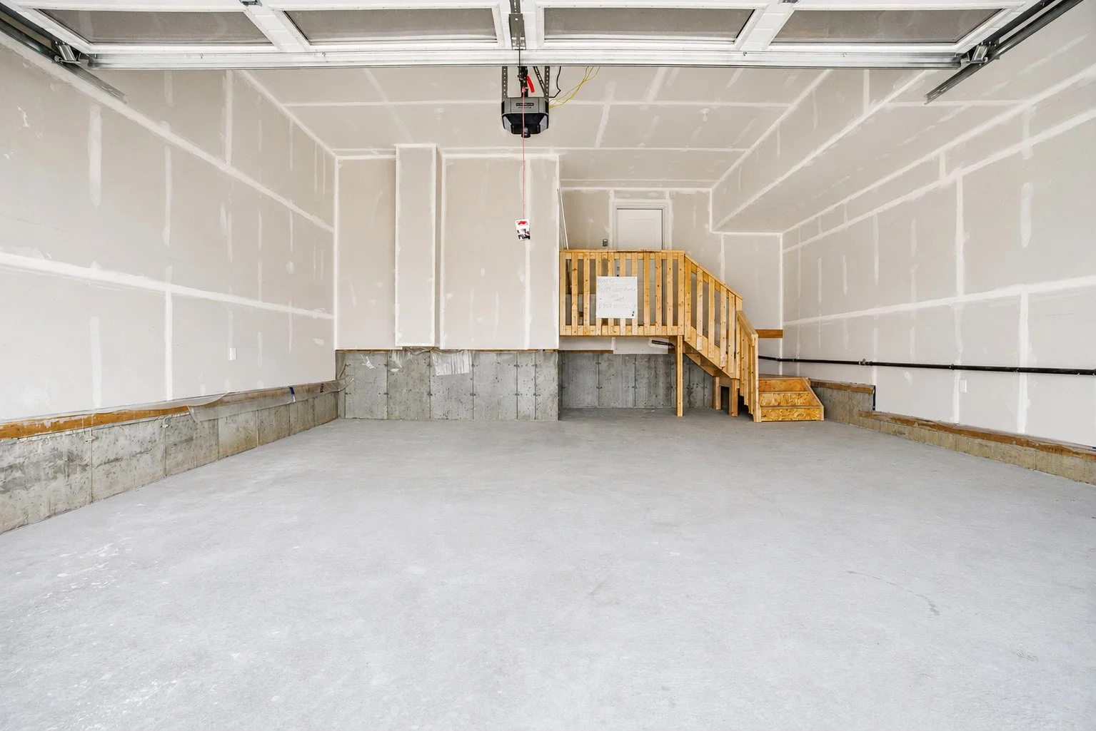Empty garage with unfinished walls, concrete floor, and a wooden staircase leading to a door at the back.