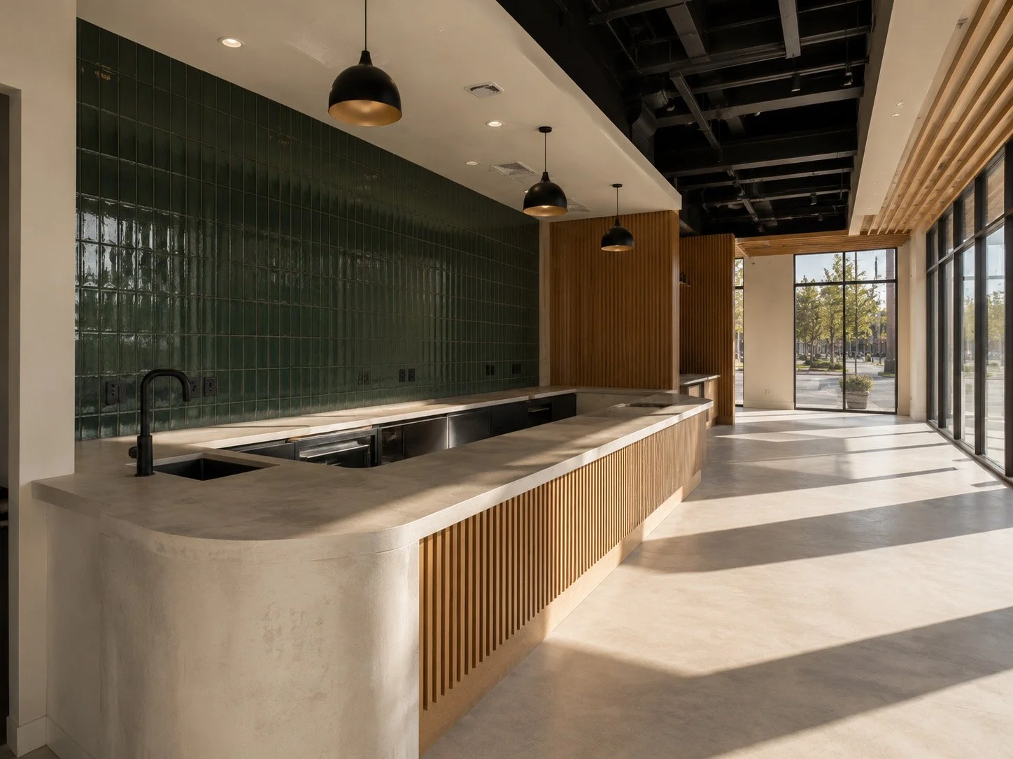 Modern interior with a curved marble kitchen island, black sink faucet, dark green tiled backsplash, black pendant lights, wooden accents, and large floor-to-ceiling windows letting in natural light.