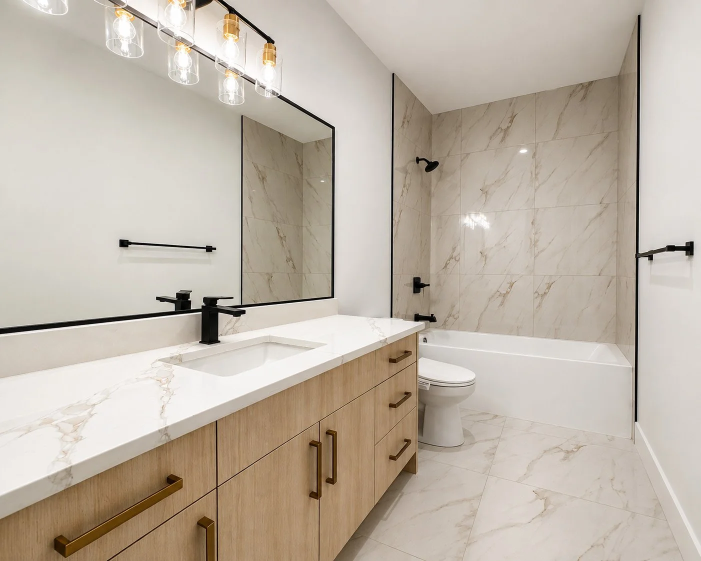 Modern bathroom with a wooden vanity, black fixtures, large mirror, marble walls and floor, white bathtub, and toilet.