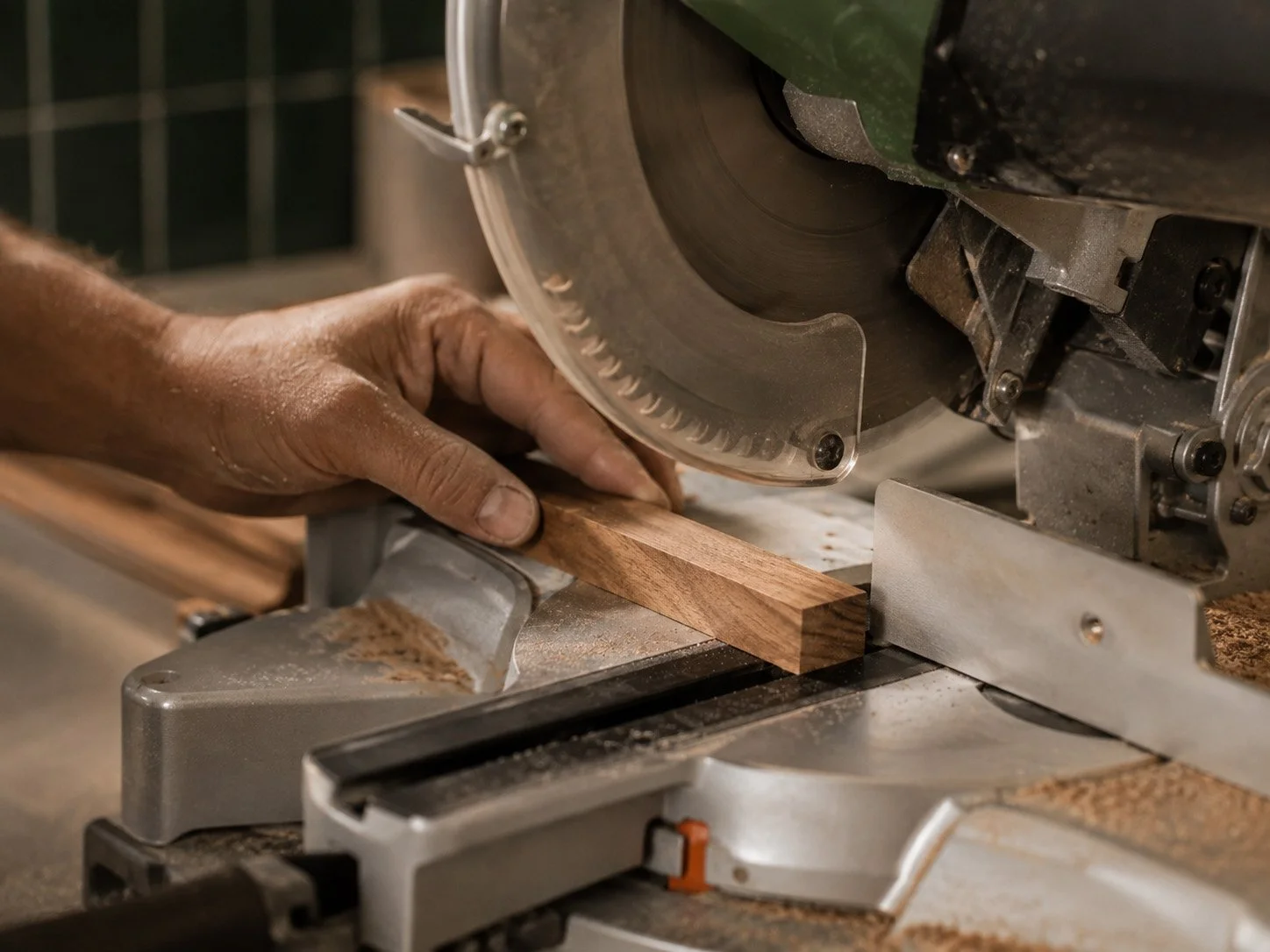 A person working with a miter saw cutting a piece of wood in a woodworking shop.