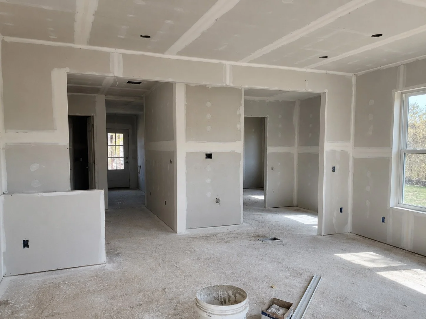 Interior of a house under construction with unfinished drywall, visible installation holes, and construction materials on the floor.