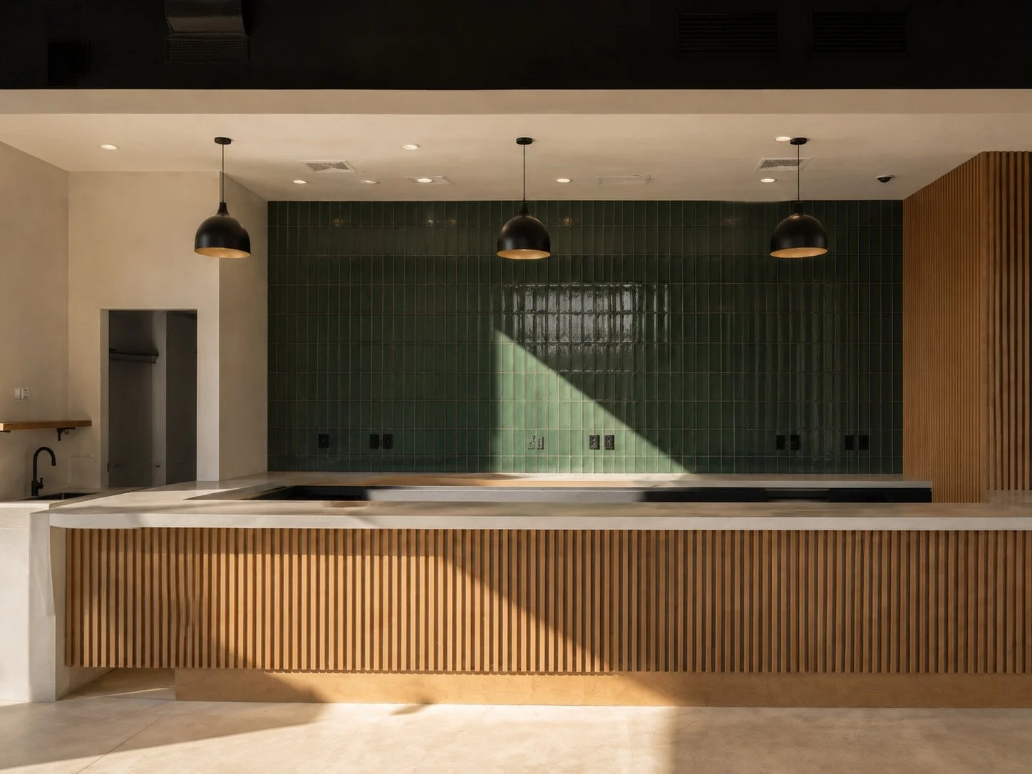Modern kitchen with a green tiled wall, wooden slatted cabinets, black pendant lights, and a white marble countertop.