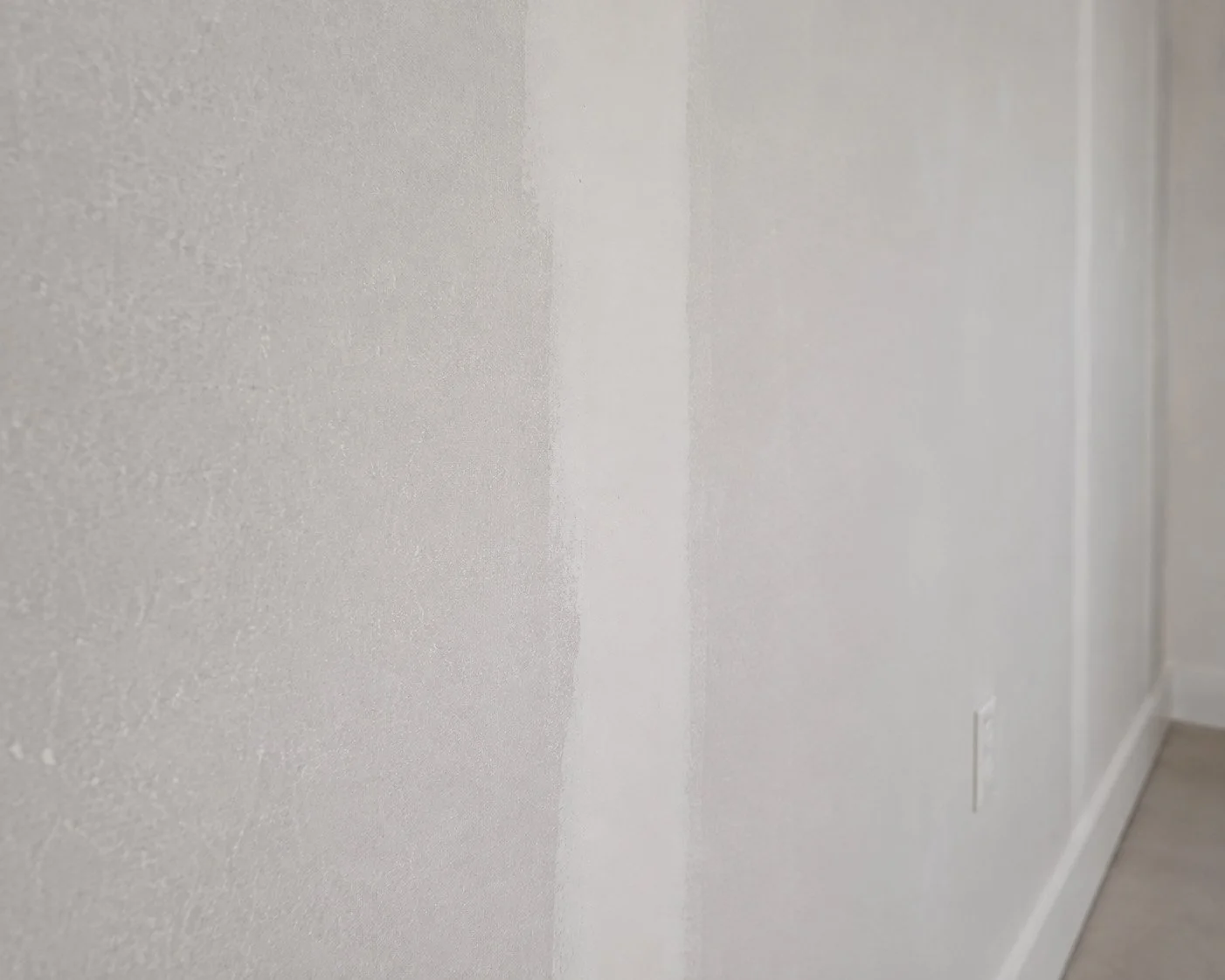 Close-up of a textured white wall with at least two sections painted with a lighter shade, showing the edge where the paint change occurs.