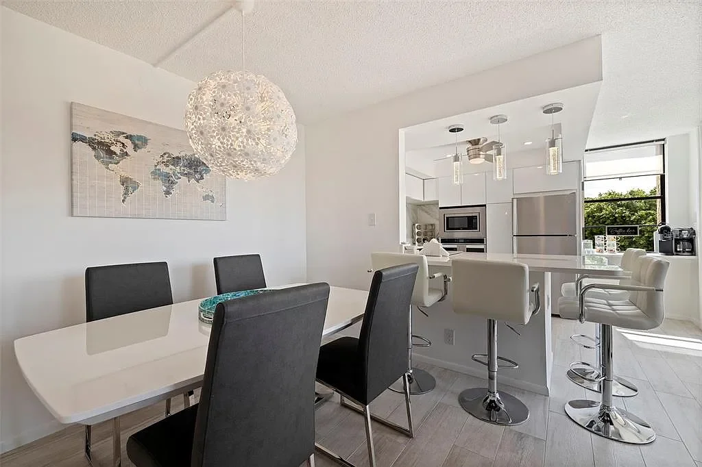 Modern kitchen with white cabinets, bar stools, and a dining table with six black and white chairs. A world map wall art and a spherical light fixture are visible. For a luxury accomodation