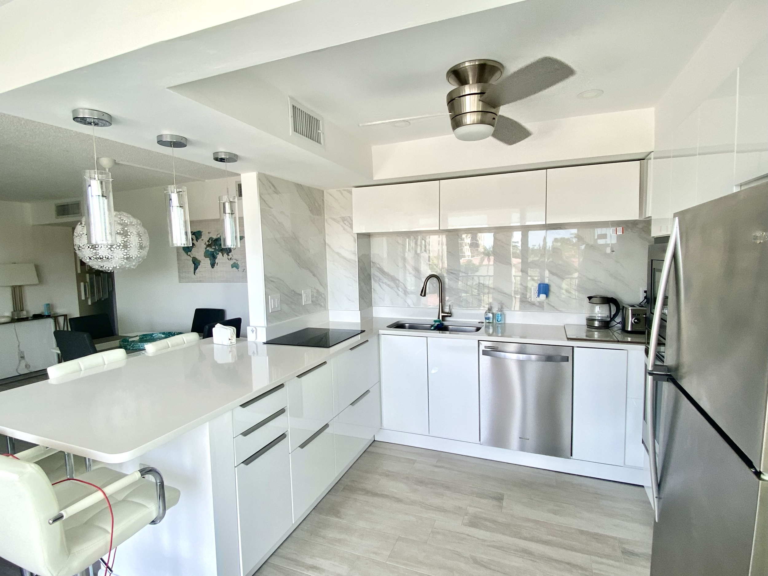 Modern well equipped white kitchen with marble backsplash, stainless steel appliances, and a large island. Ceiling fan and pendant lights are visible. For a luxury accomodation