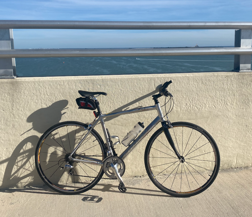 Cannondale Alu / carbon lightweight Silver road bicycle leaning against a beige wall with a metal railing, shadow cast on the wall, water and sky in the background. Complimentary use of quality specialist bicycles / bike.