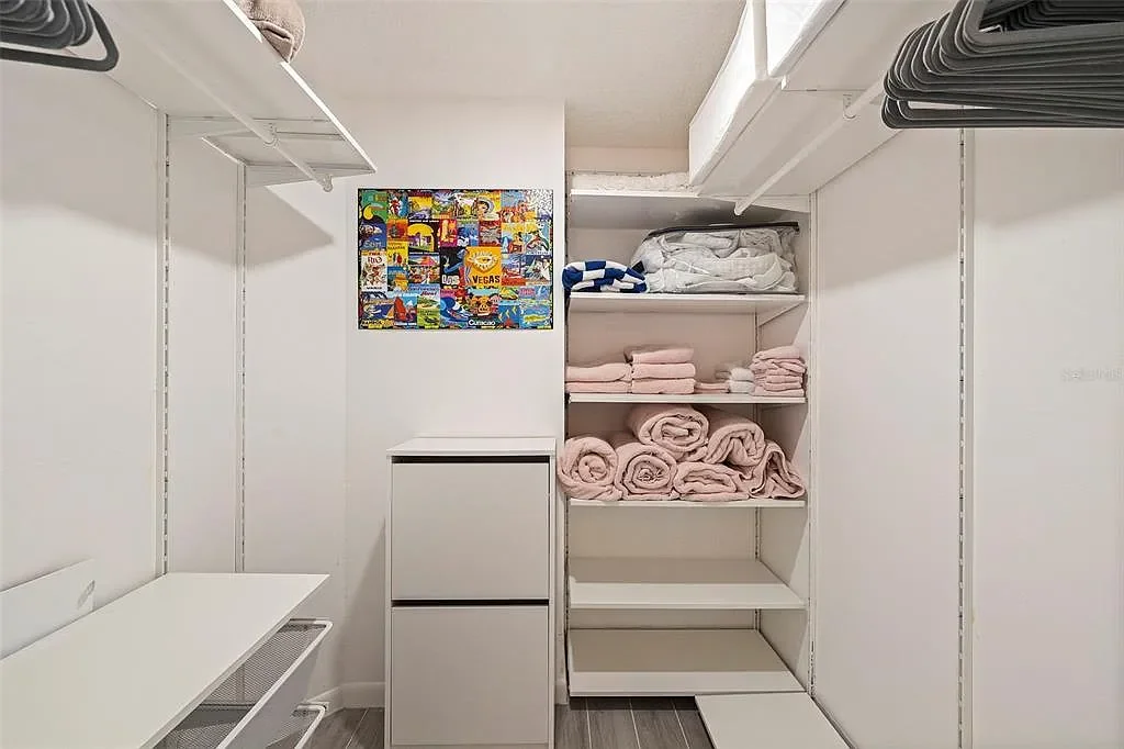 Clean closet with folded pink towels, white linens, and a small cabinet on a white wall.