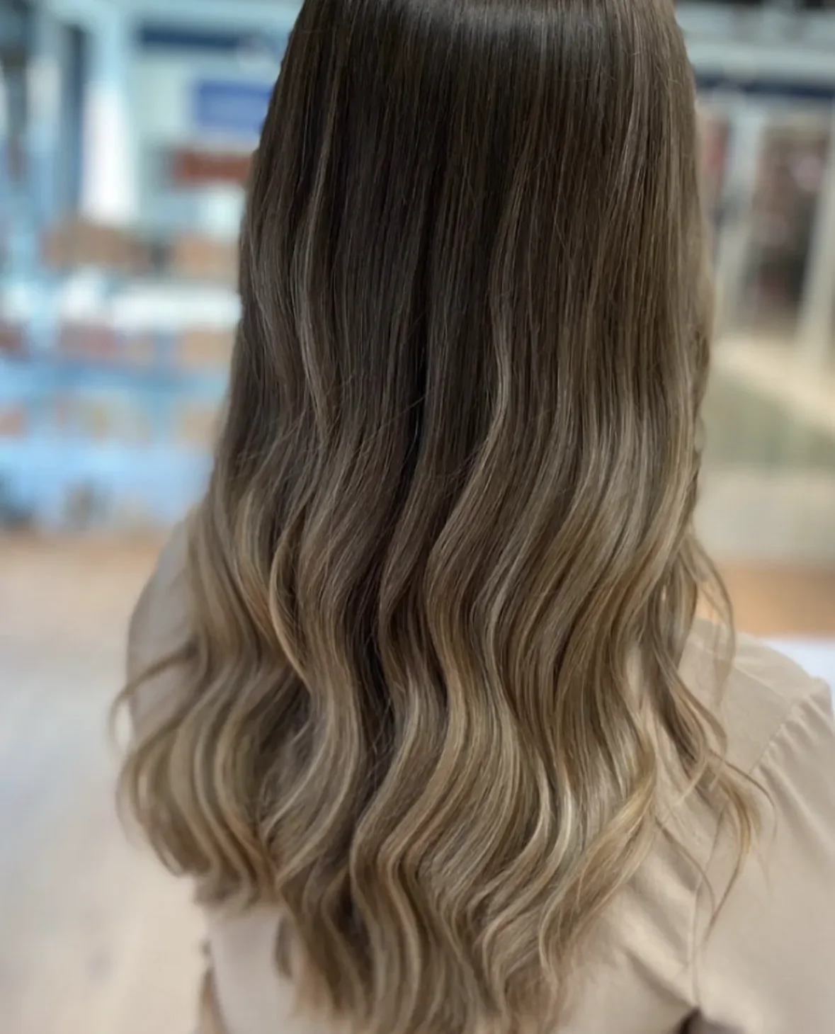 Billedet viser en person med langt, bølget, lysebrunt hår med lyse highlights i en frisørsalon.