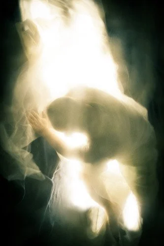 Silhouette of a person kneeling or crouching, surrounded by smoke or fog, with light shining behind.