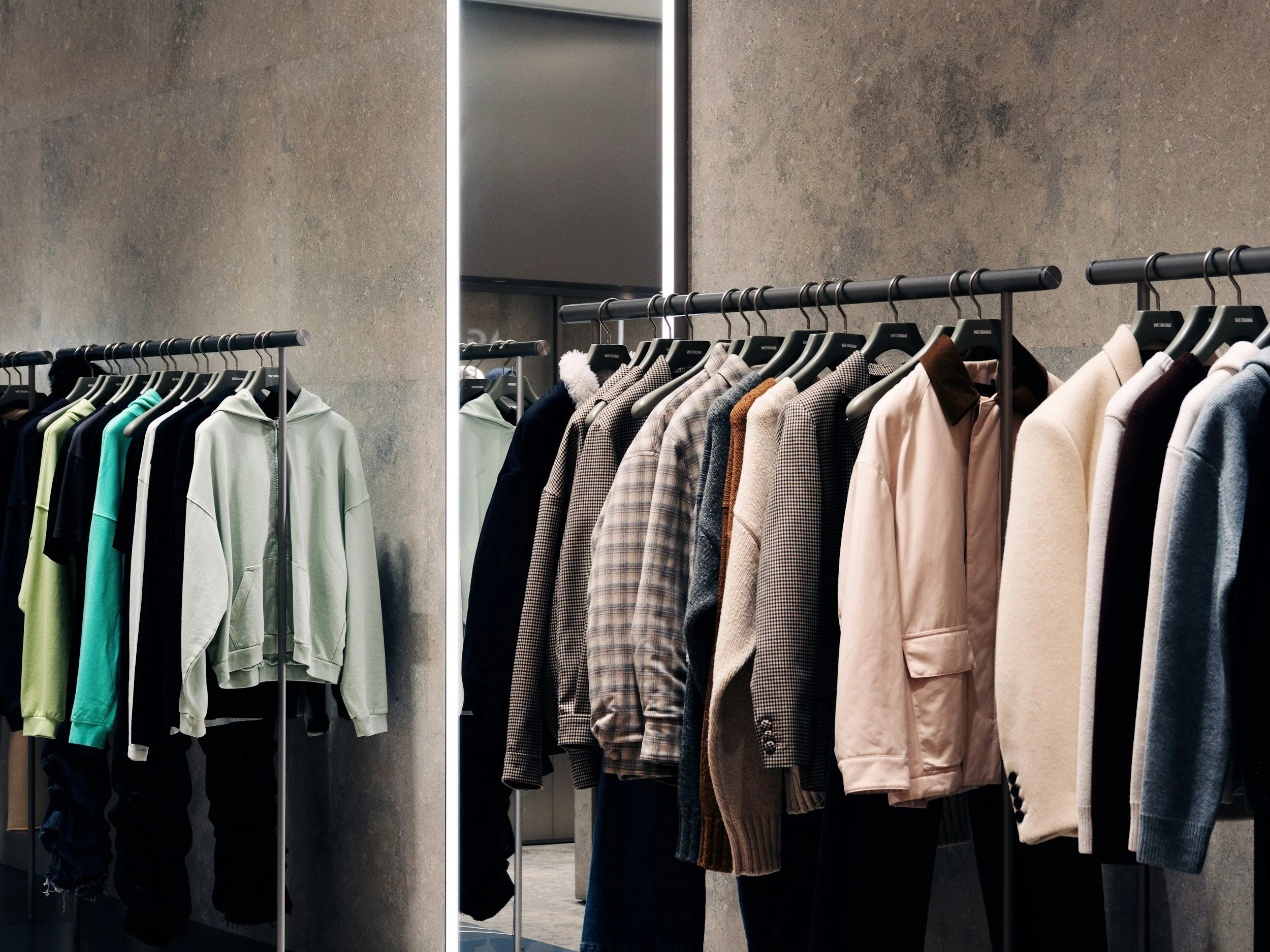 Clothing store shelf with hoodies and jackets on black hangers against a gray concrete wall.