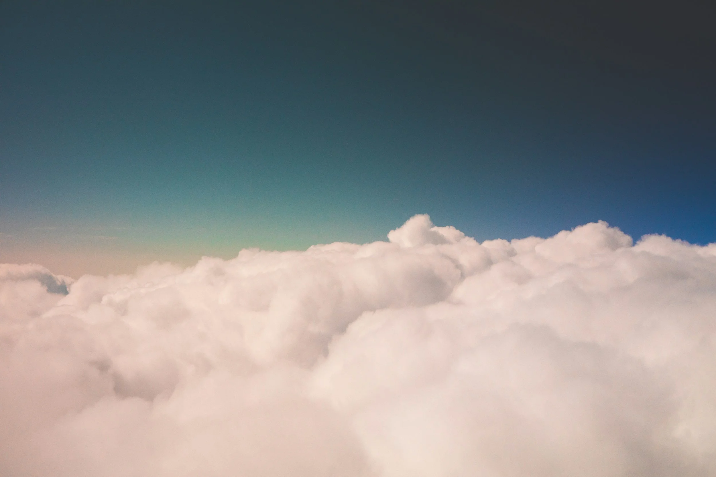 View of fluffy white clouds from above, with a gradient blue sky above.