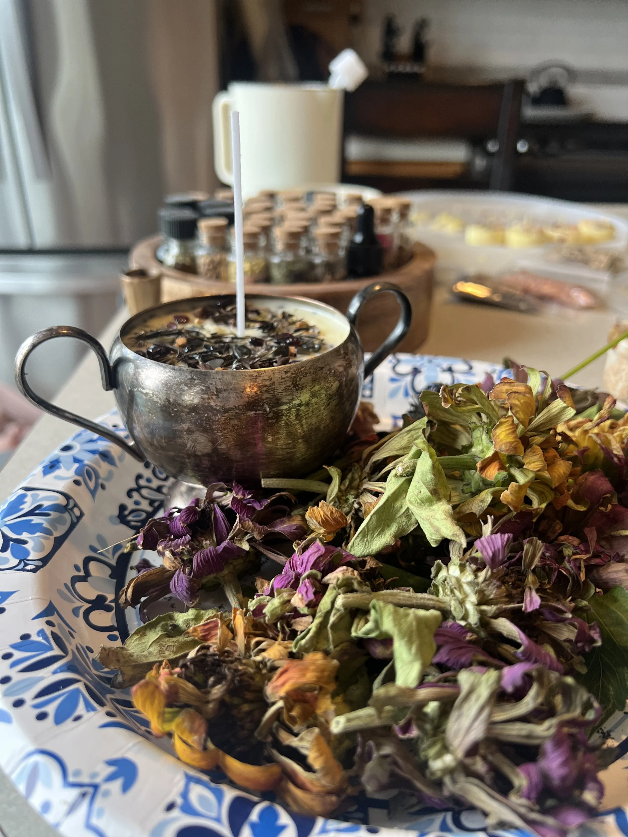 A metal teapot with a white straw in it, surrounded by dried flowers, on a blue and white patterned disposable plate.