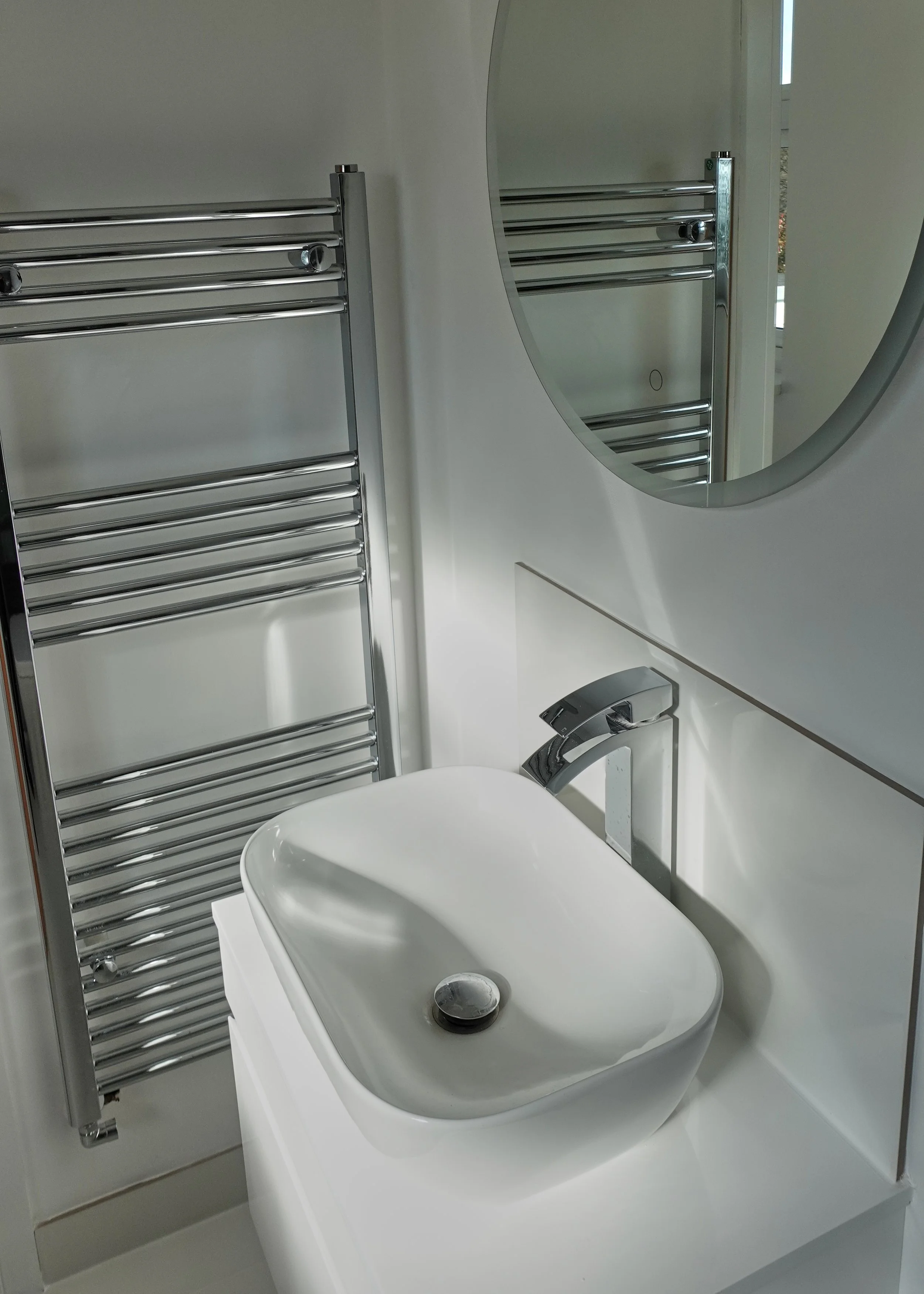 A bathroom sink with a chrome faucet, mirror, heated towel rack, and window.