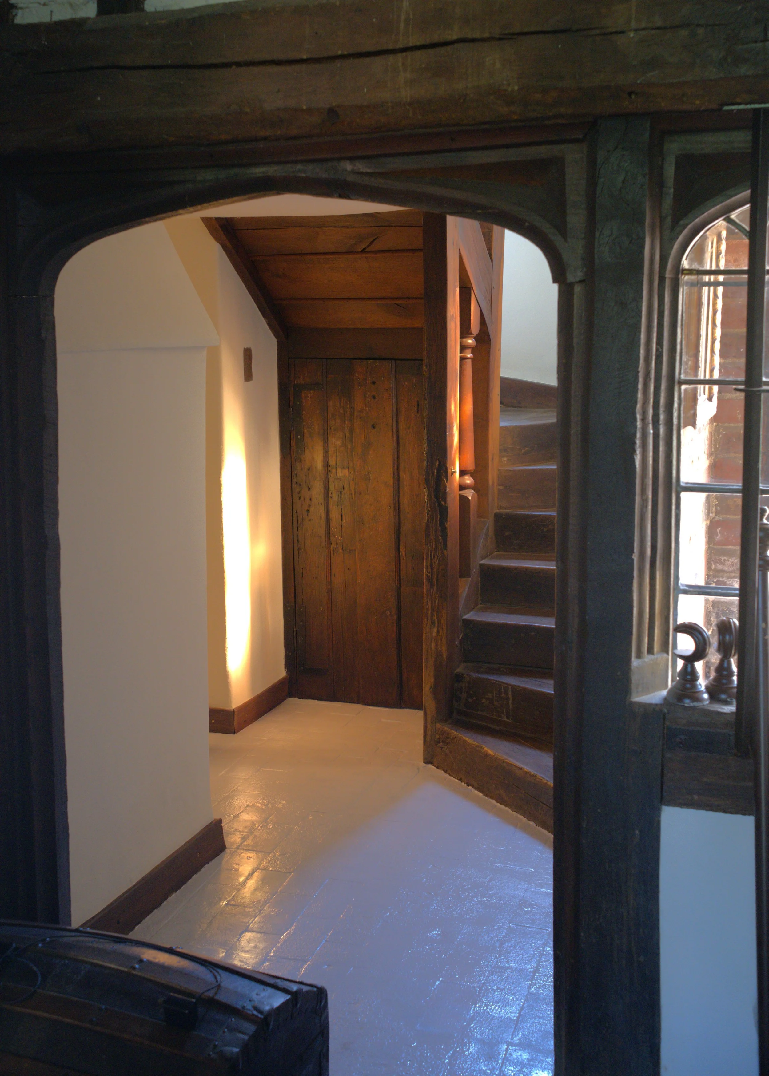 View through a rustic wooden doorway showing a staircase and a cozy interior with white walls and warm lighting.