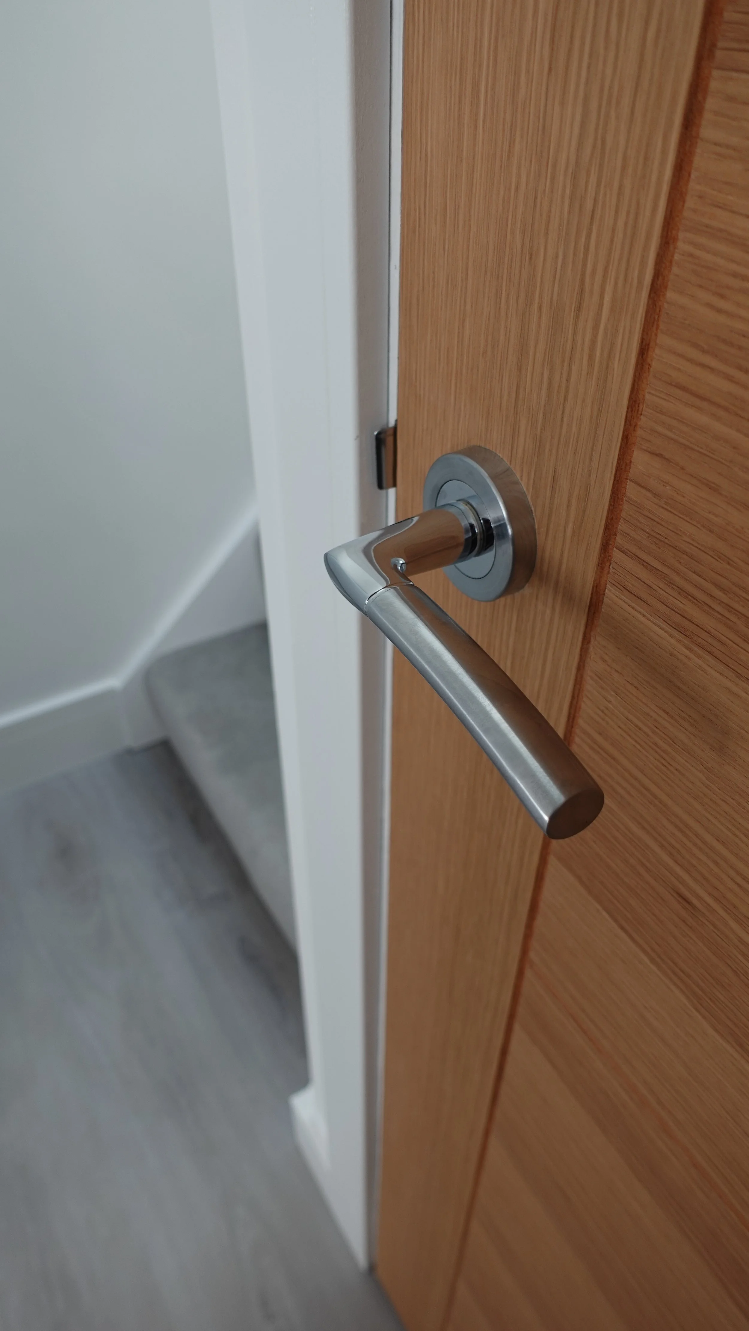 Close-up of a modern silver door handle mounted on a wooden door.