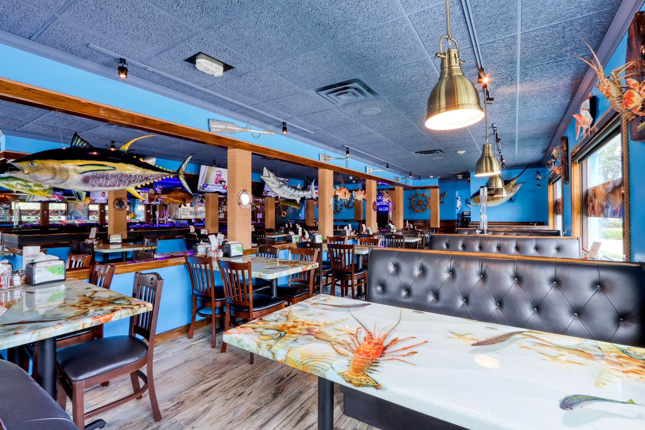 Interior of a seafood restaurant with blue walls, hanging fish and lobster displays, and tables with lobster-themed tablecloths.