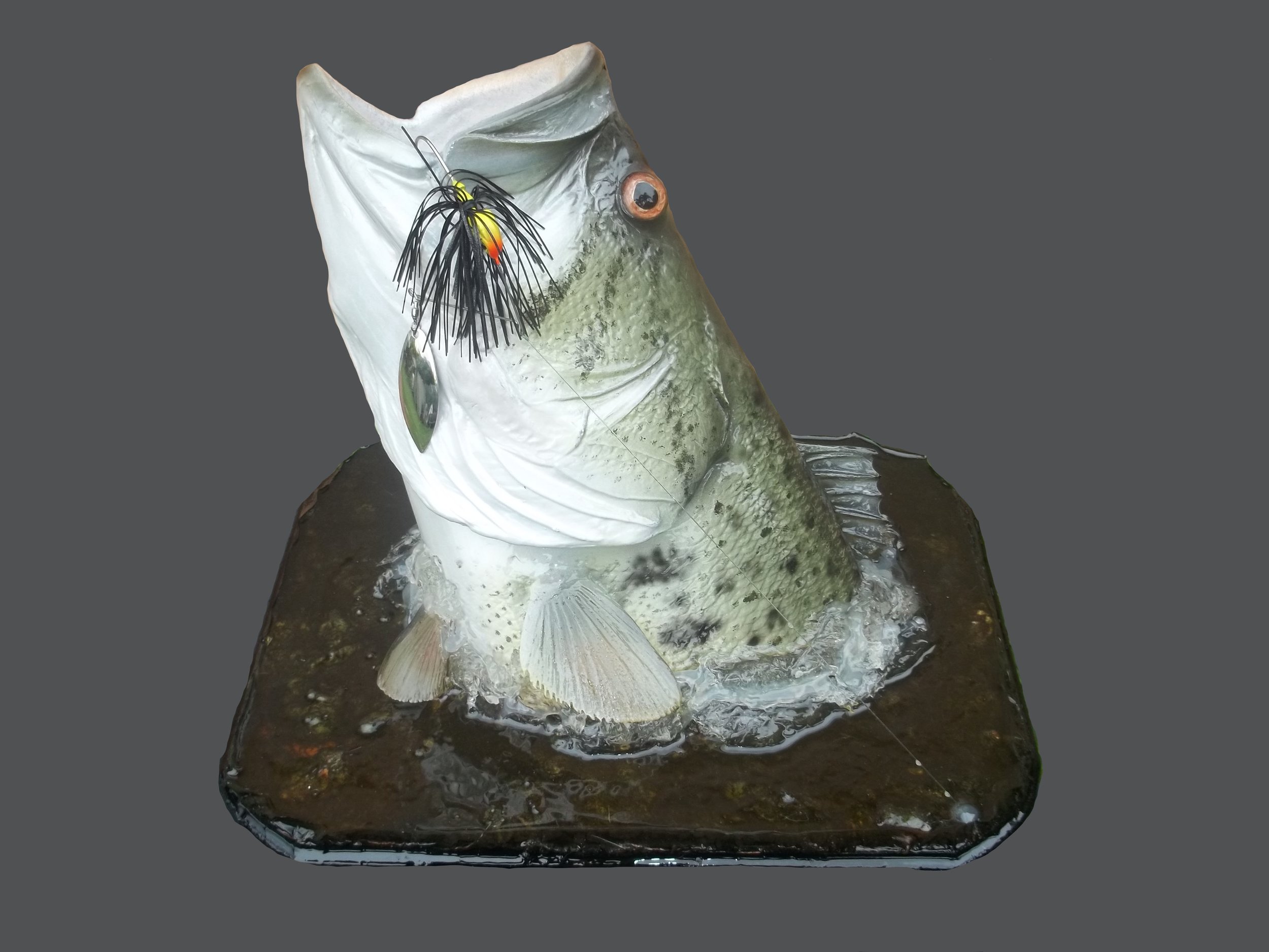A mounted largemouth bass fish with a fishing lure in its mouth, set on a dark base with water and ice.