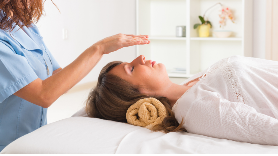 A woman lying on a treatment table with a towel under her head, receiving a forehead massage from a healthcare professional.