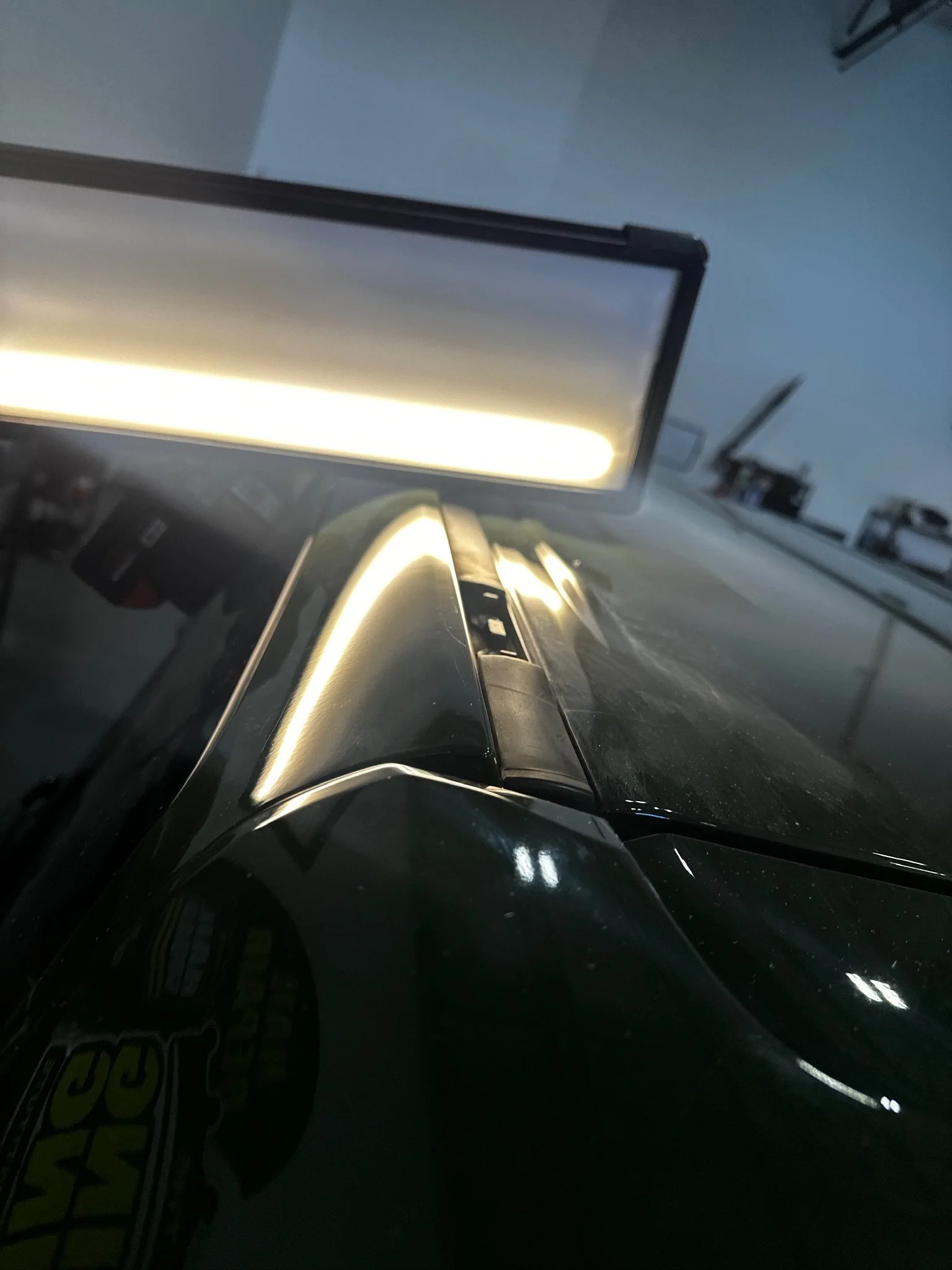 Close-up of a black vehicle, possibly a car, with a reflection of light on its surface. There are some objects and a board visible in the background.