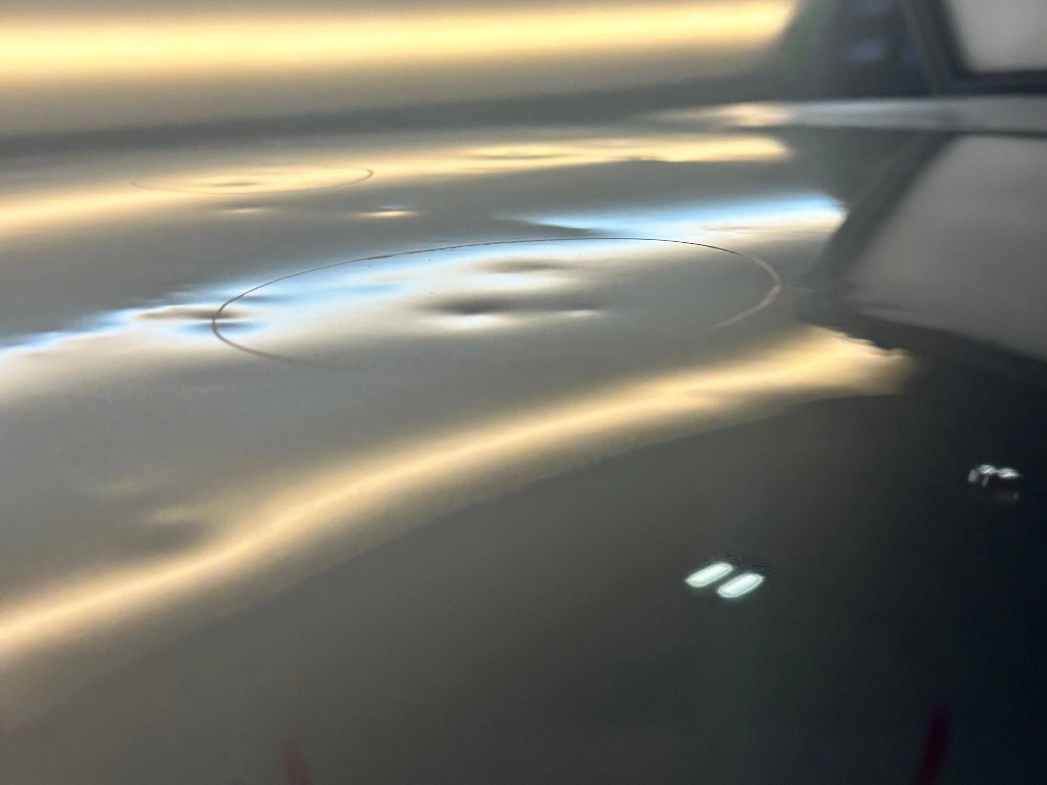 Close-up of a metallic surface with laser-engraved outlines of shapes and reflections of light.