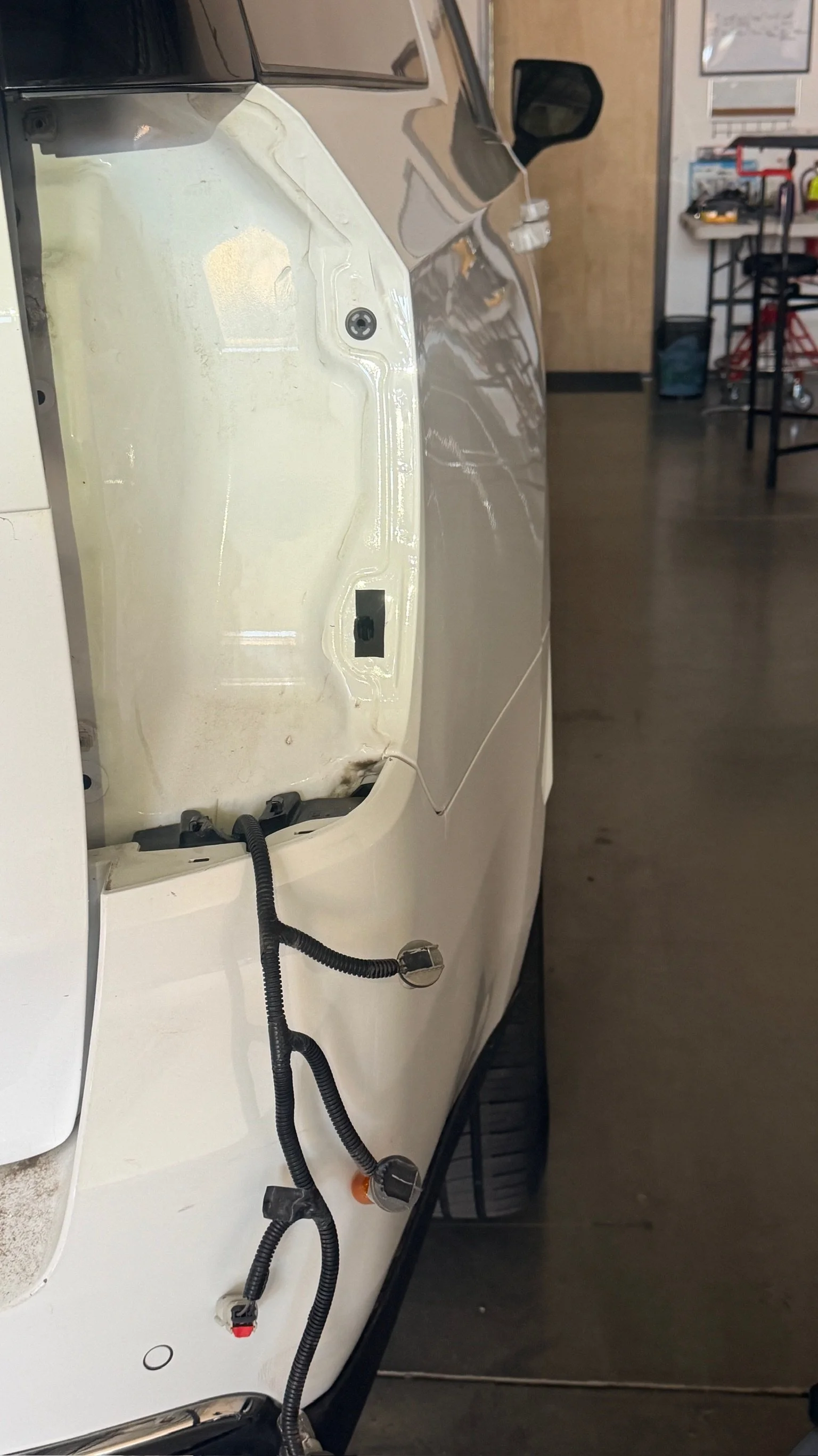 The image shows a white car with its hood open, exposing the engine bay. The car is parked indoors, possibly in a garage or workshop.