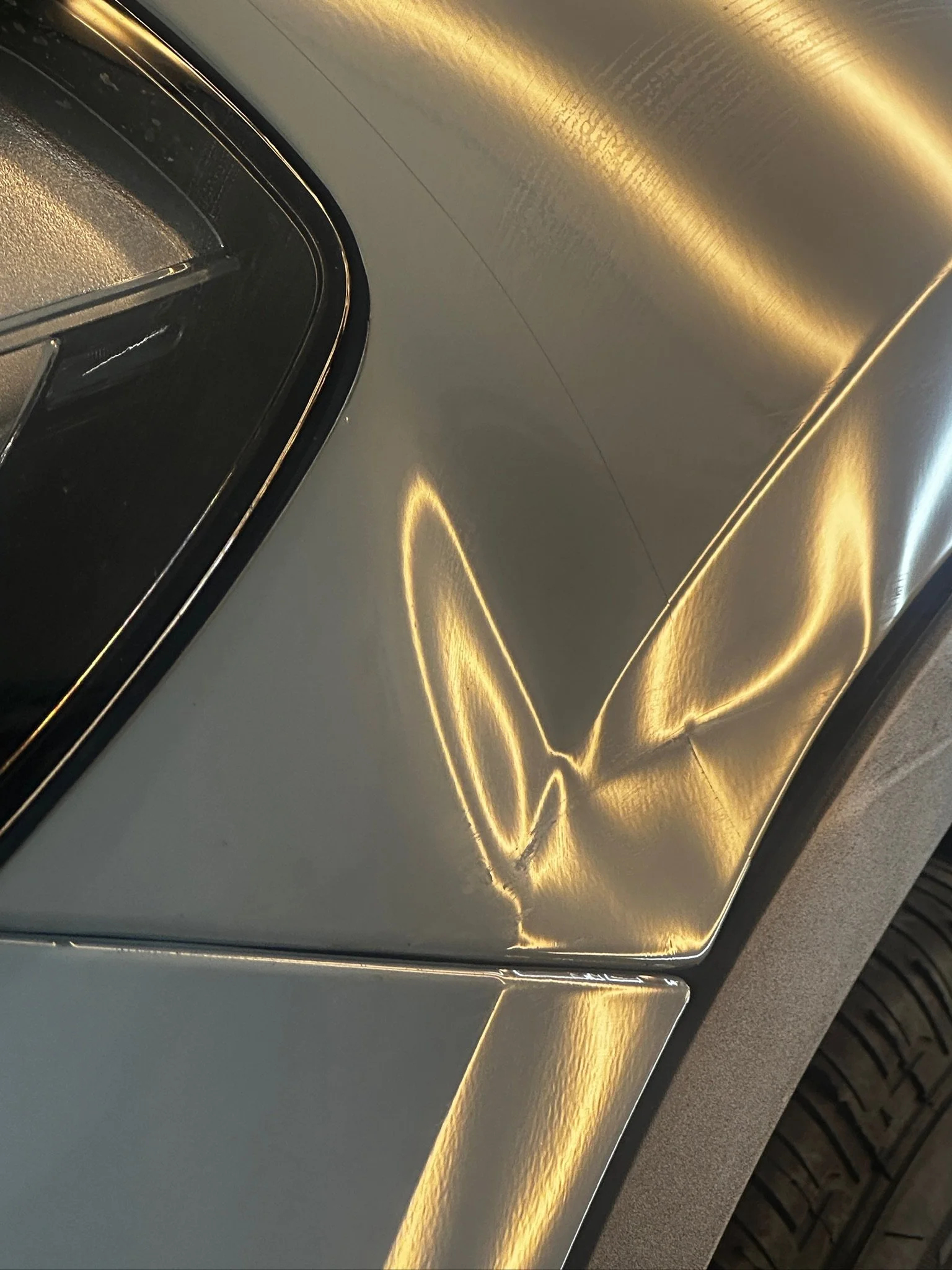 Close-up of a silver car's body with a visible scratch and reflections of light.