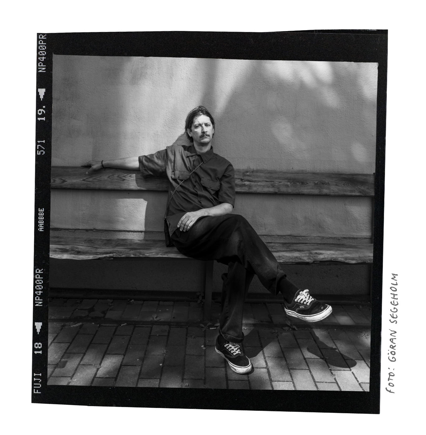 Photo of Martin sitting relaxed on a bench in the early summer sun with some shade from a close by tree.