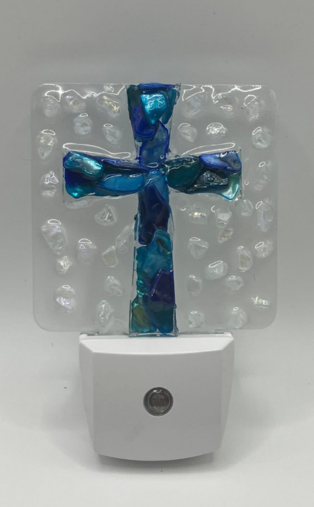 A blue and green glass cross mounted on a clear backdrop with bubble-like textures, placed above a white scale showing 0.00 pounds.