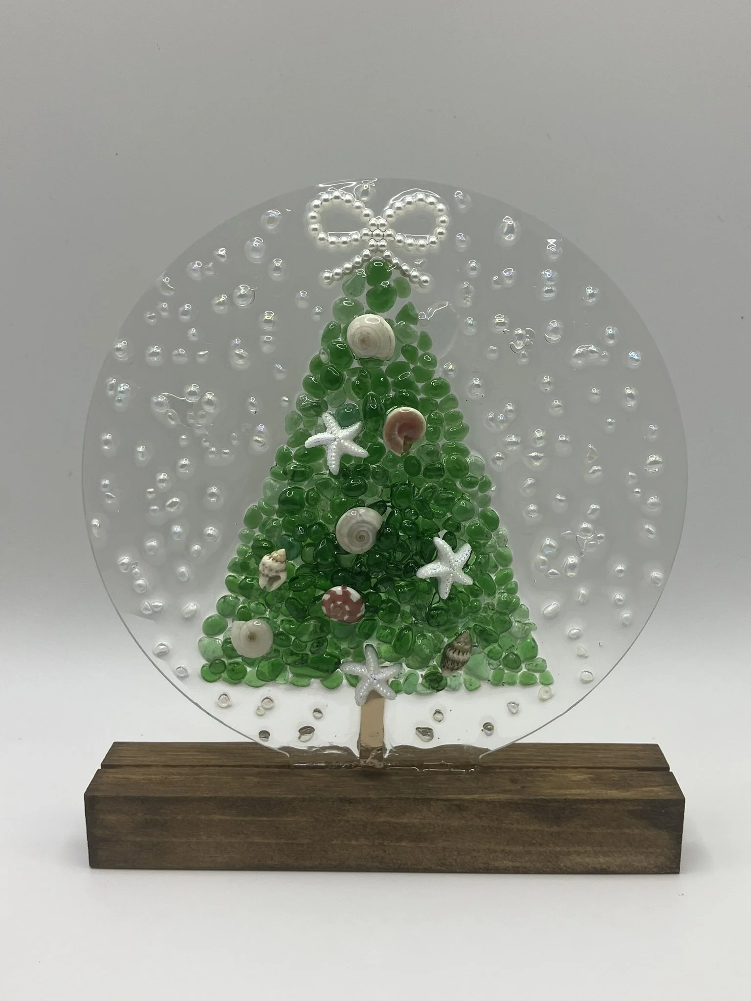 A decorative Christmas tree made of green glass beads, shells, starfish, and seashells, mounted on a wooden base with a transparent circular cover.