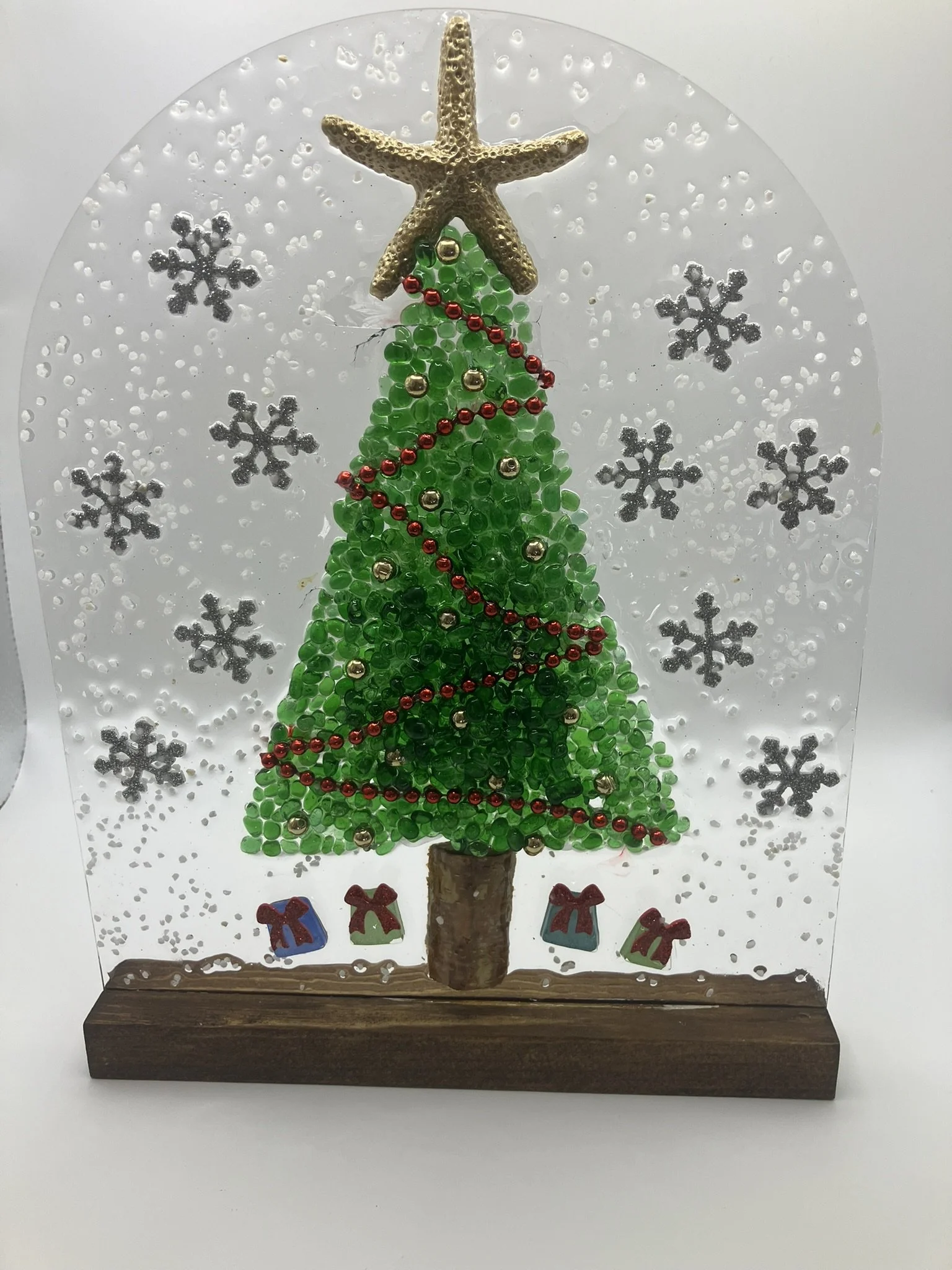 A crafted Christmas scene with a starfish and beads forming a Christmas tree on a wooden base, decorated with small ornaments and surrounded by snowflake decorations.